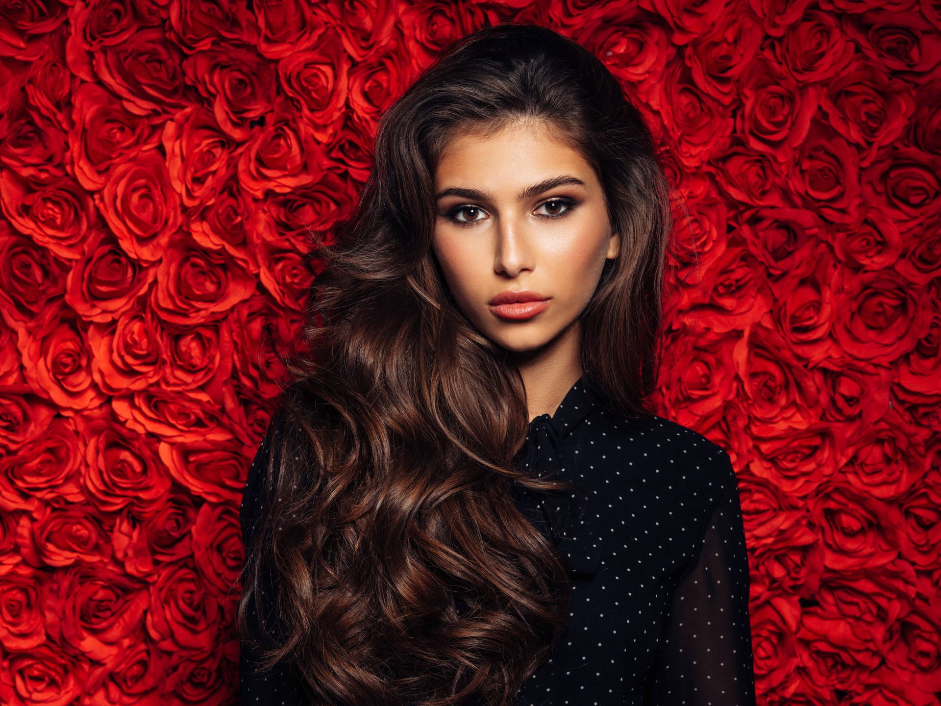 Elegant Woman Posing Against a Rose Wall with Vibrant Red Background